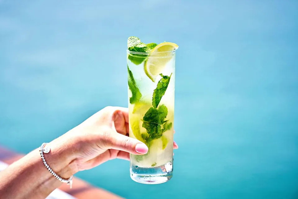 An alcohol-free cocktail with lime and mint pictured against a blue sea